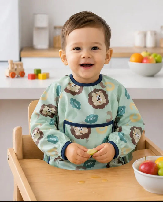 Petit garçon souriant sur une chaise haute portant un bavoir intégral à manches longues vert d'eau à motifs de lion,