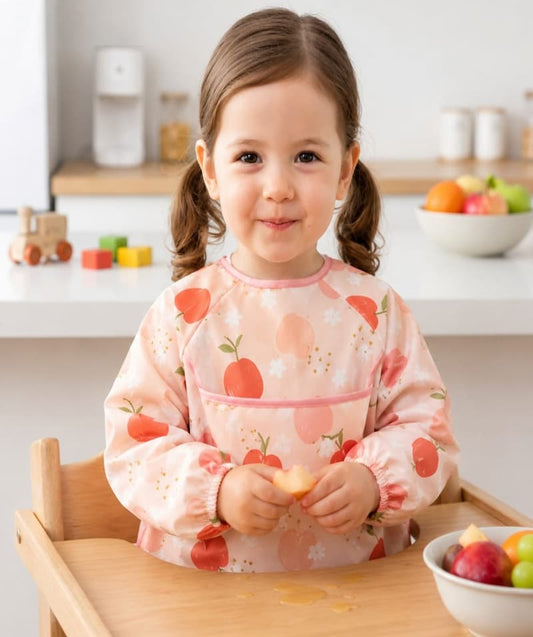 Petite fille sur une chaise haute portant un bavoir intégral à manches longues rose imperméable pour le repas,